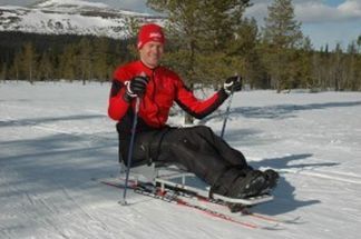 Man i røde klær sitter på kjeke med ski på vinteren